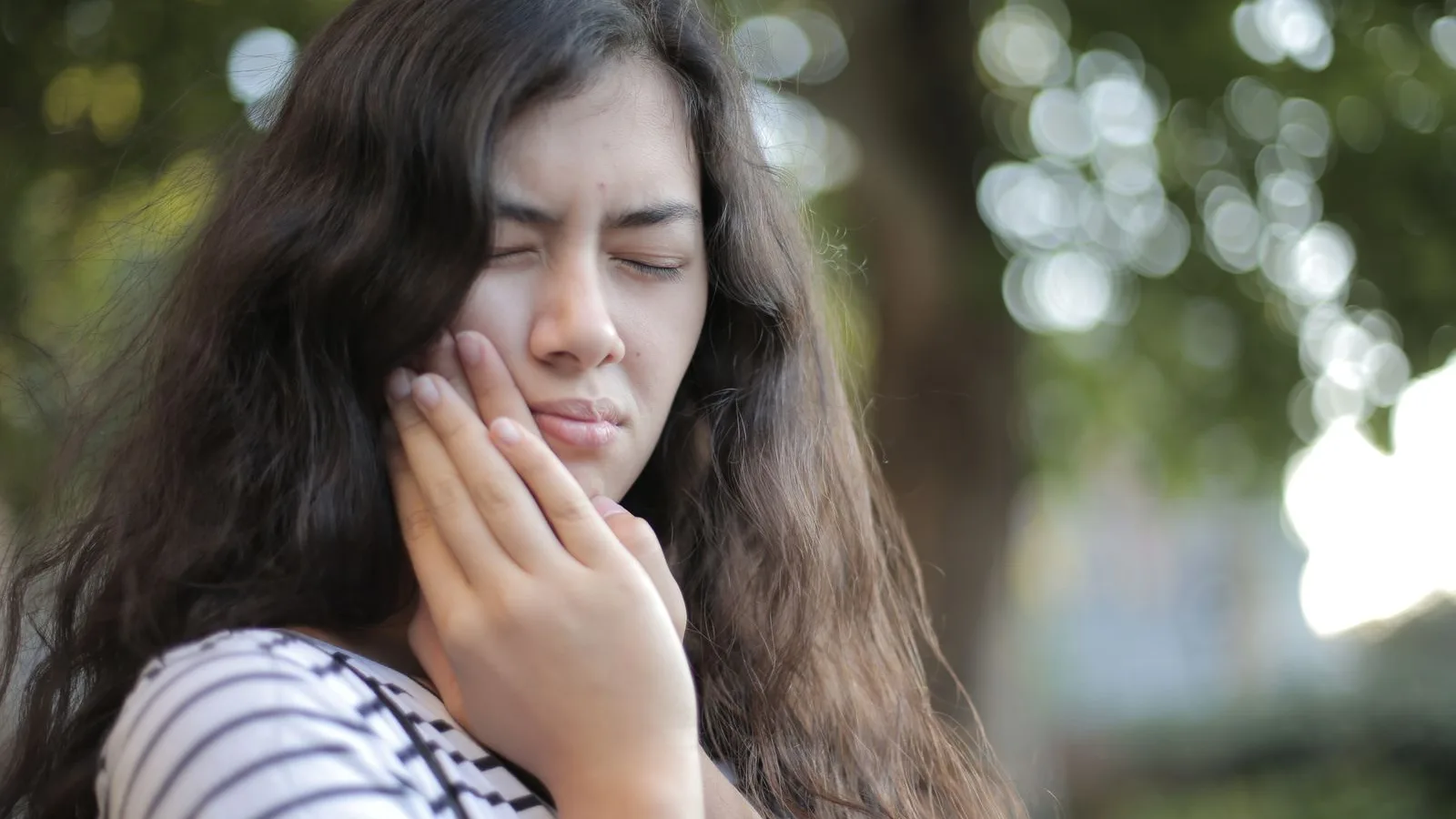 Traveler outdoors holding her cheek in discomfort from a toothache