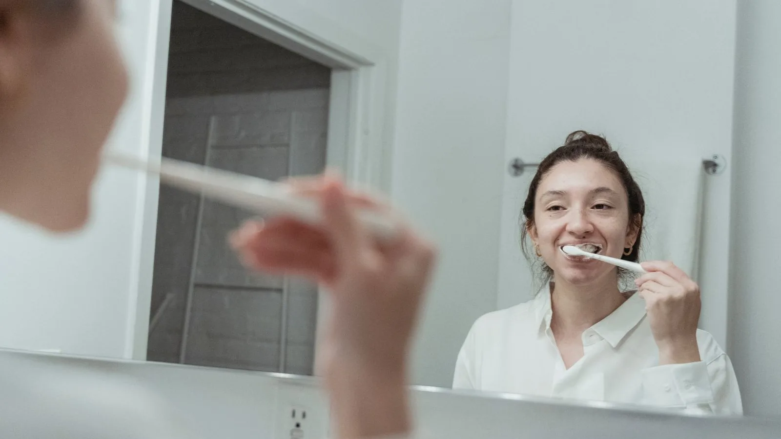 Woman brushing her teeth at a bathroom mirror during her morning routine